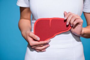 Woman in white holding a paper illustration of a liver against a blue background - Standard CBD
